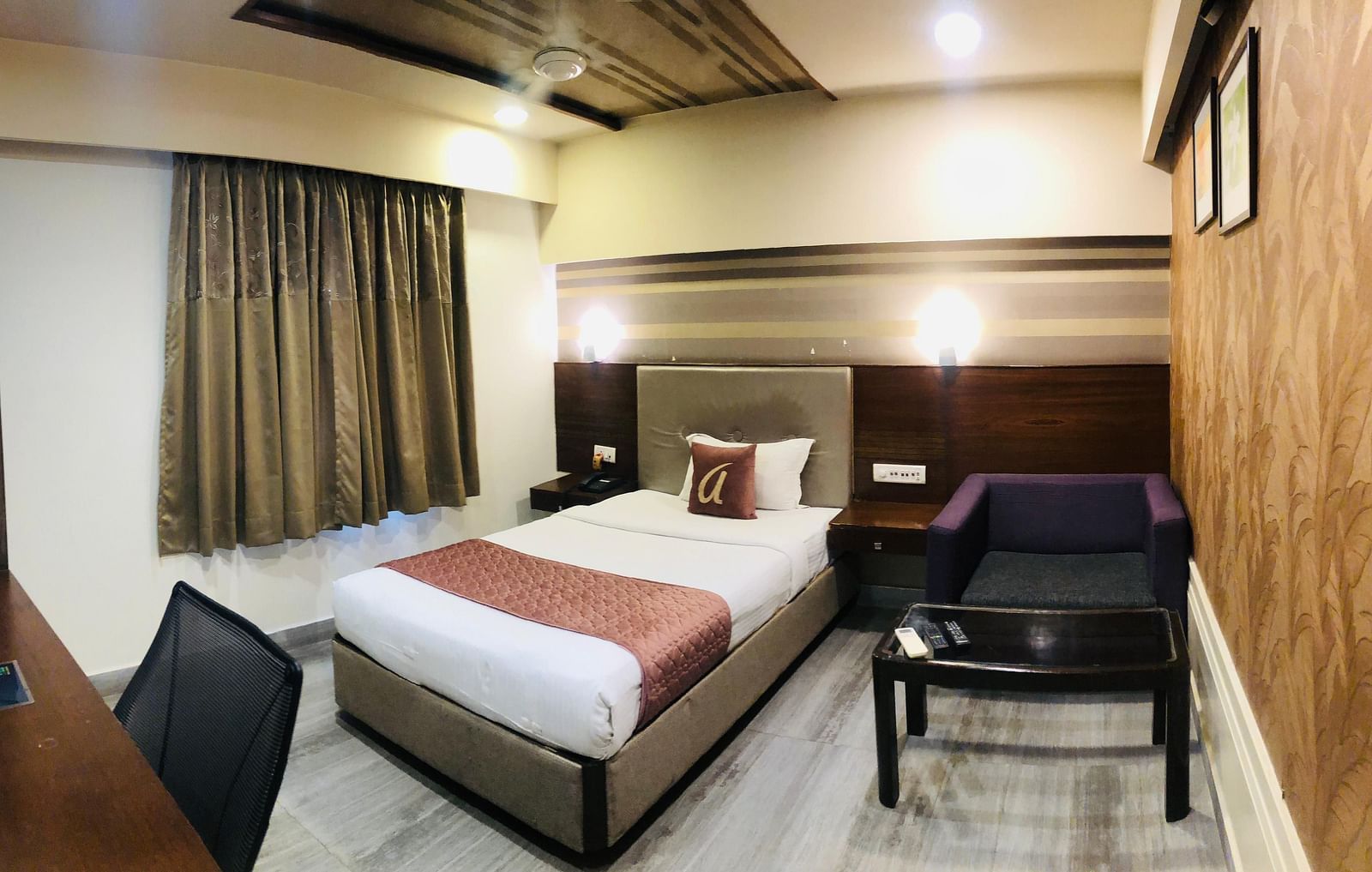 Comfortable single room in a hotel featuring a neatly made bed with a maroon runner, a work desk with a computer, and a small seating area | Astra Hotels and Suites Kadubeesanahalli
