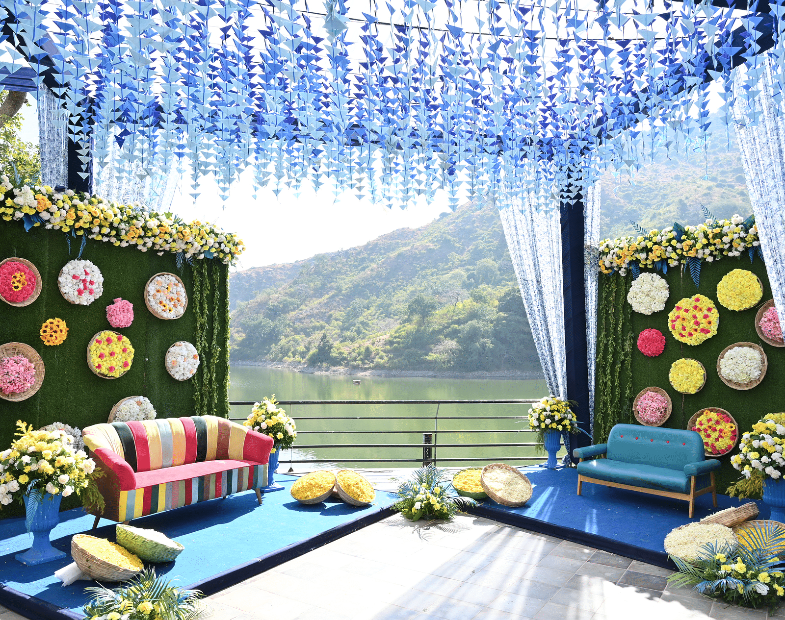 Blue floral mandap with colourful sofa seating and green hills as a backdrop - Via Lakhela Resort & Spa