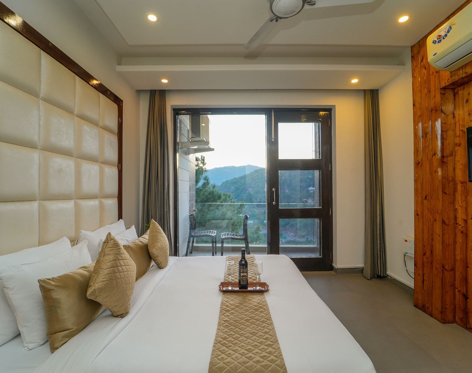 The premium room at DLS Whispering Winds, Kasauli, featuring a bed with plush bedding and the glass door leading to the balcony with the mountain view.