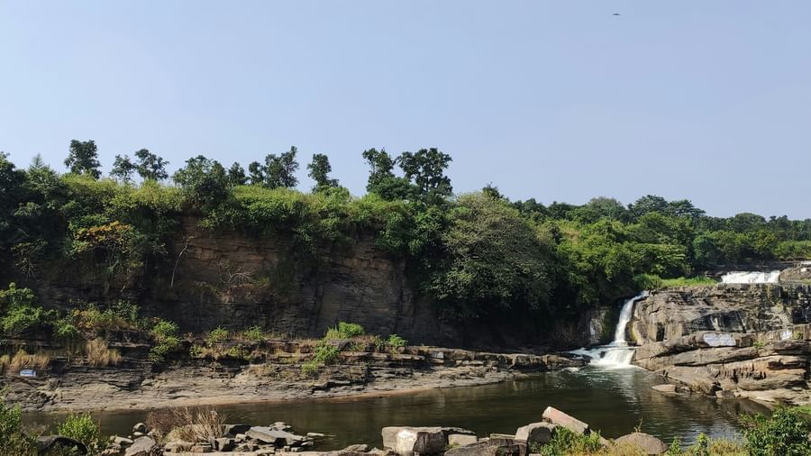 A far out view of a small waterfall converging into a waterbody with rocks and greenery in view - Dhanbad Famous Places