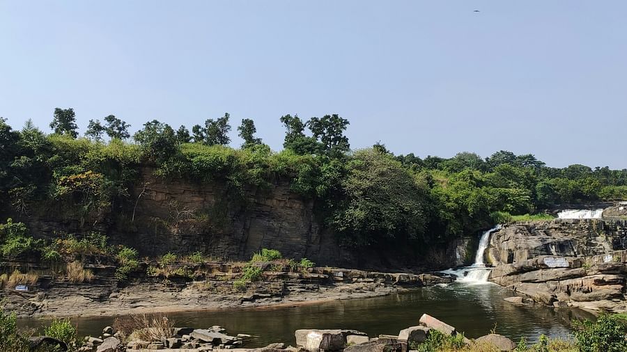 a small waterfall being collected in a waterbody with trees in the background