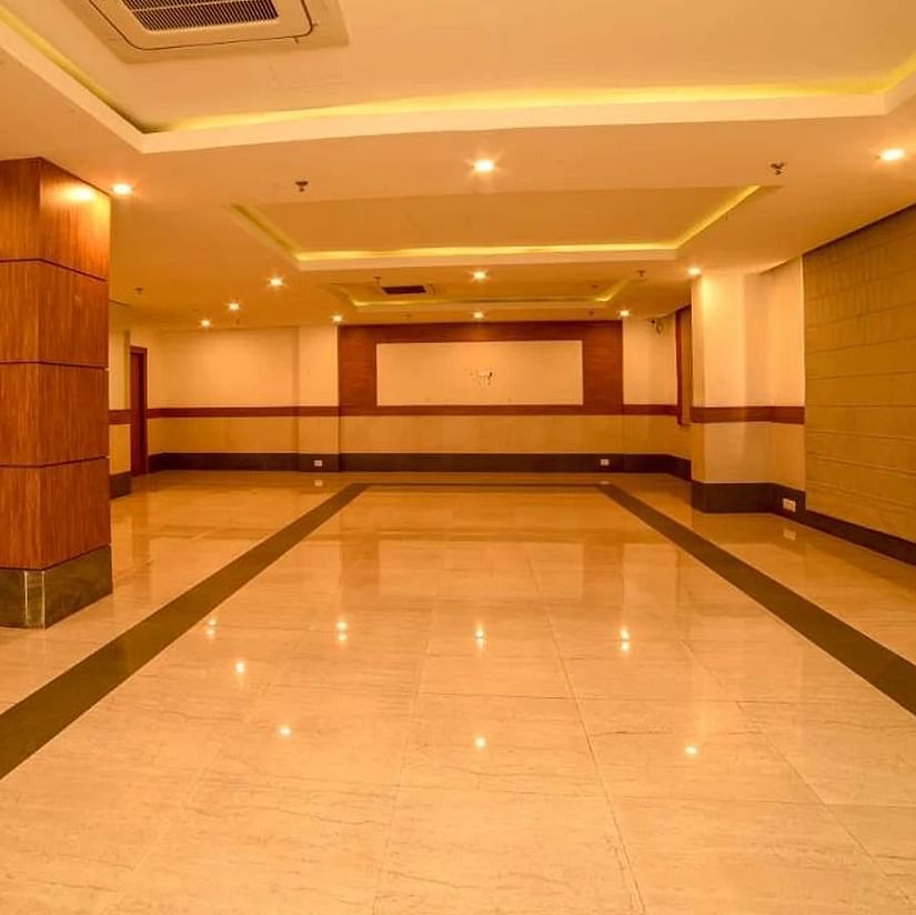 An image of a spacious banquet hall with installed lights in the ceiling - An image of a reception lobby featuring a reception desk , and a seating area for the guest - Max Hotel Jabalpur