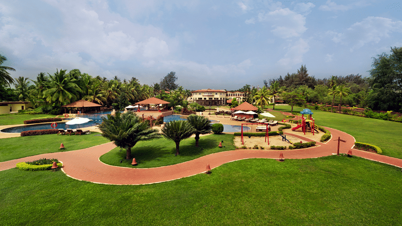 Kenilworth Resort & Spa, one of the Goa resorts on the beach, featuring manicured lawn with pavements under a blue sky