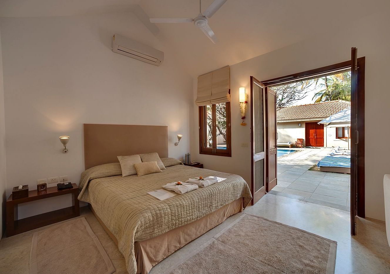 Neatly arranged bed with cushions and a view of the pool outside at Shreyas Retreat