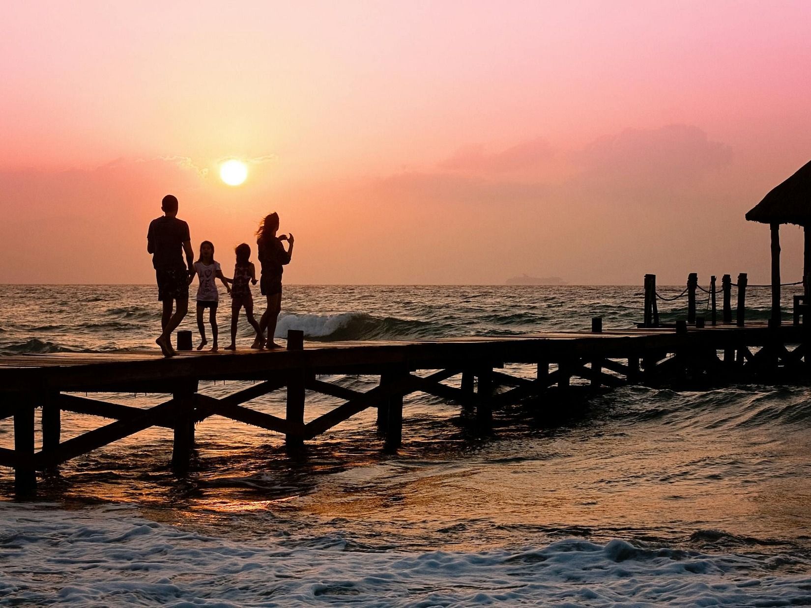 A family on a dock at sunset by the sea.