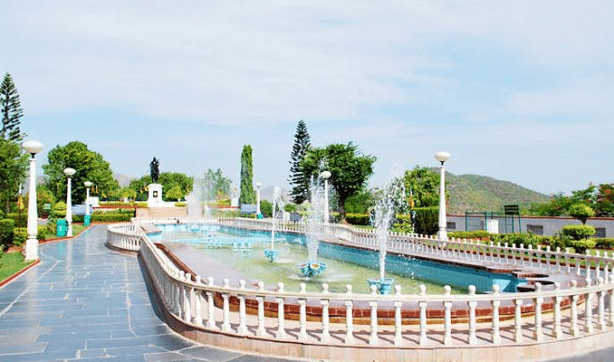 A park with a long, curved fountain, surrounded by greenery and trees. 