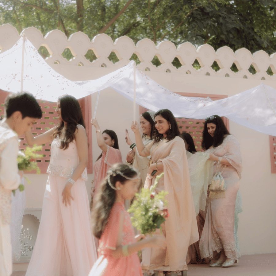 Bridesmaids carrying a white veil canopy over the bride next to a scalloped wall at Umaid Palace.
