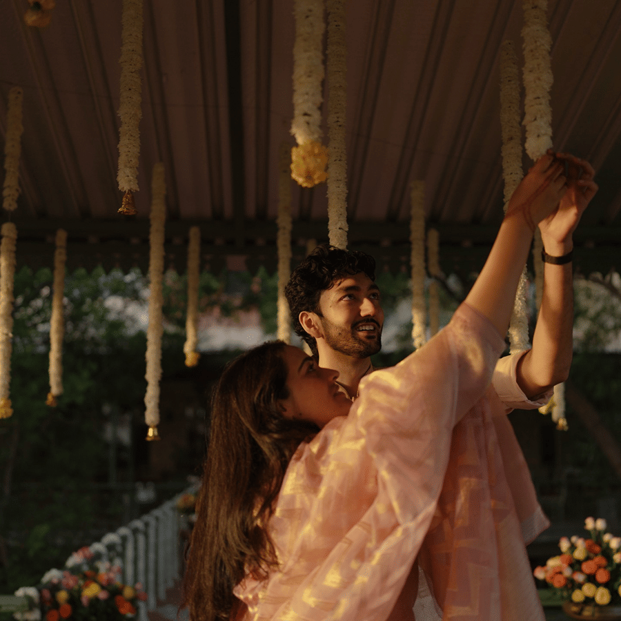 Couple sharing a candid moment together under hanging floral garlands during an evening event at Umaid Palace.