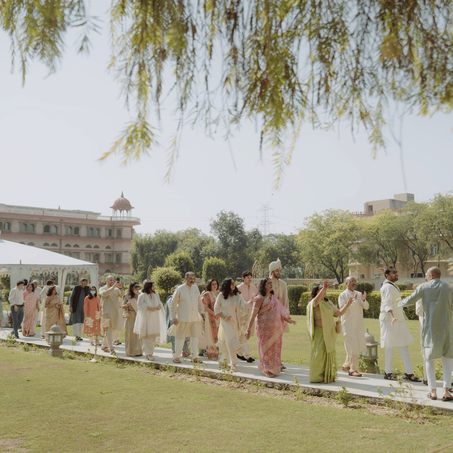 Guests in traditional wedding attire walking along a garden path with white tents on the lawn at Umaid Palace.