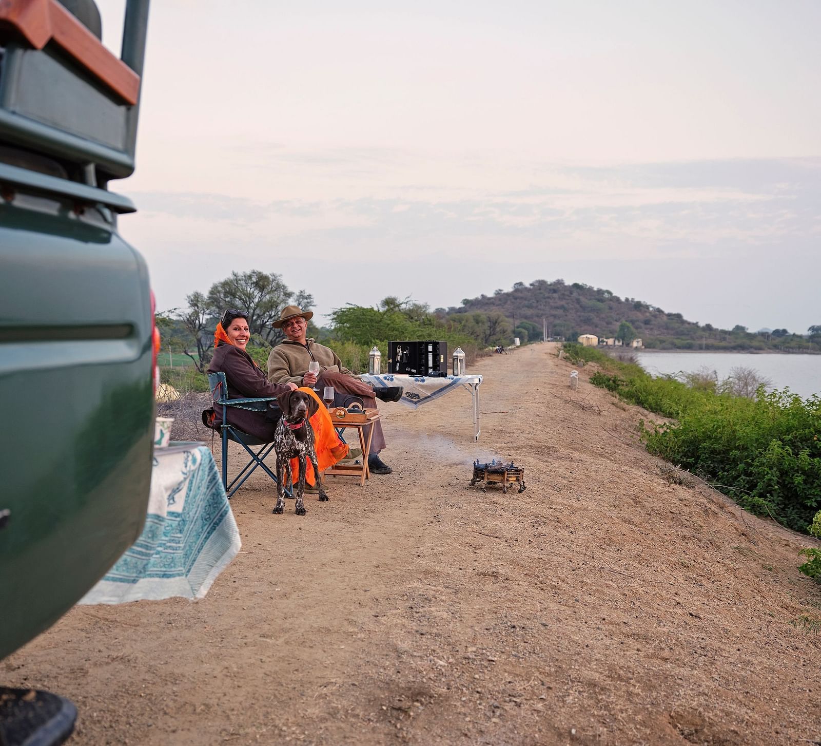 image of a couple sitting in front of the lake with a small bonfire in front of them