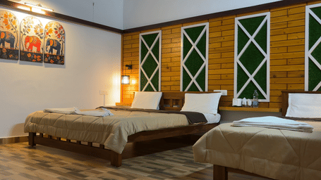 A Family Room With Garden View 2, of Hatti Eden Coorg aturing a large bed with neutral-toned linens and multiple white pillows. The headboard wall is a focal point, decorated with three vertical, rectangular panels of dark textured material accented by lig