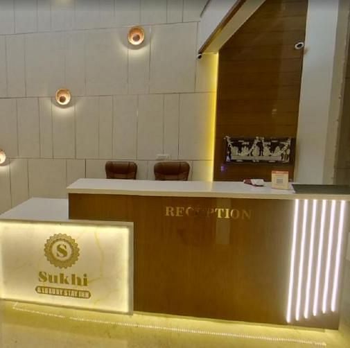 Reception area with a wooden desk featuring an illuminated logo, set against a backdrop of textured walls and ambient lighting.- Sukhi - A Luxury Stay Inn, Chikkamagaluru