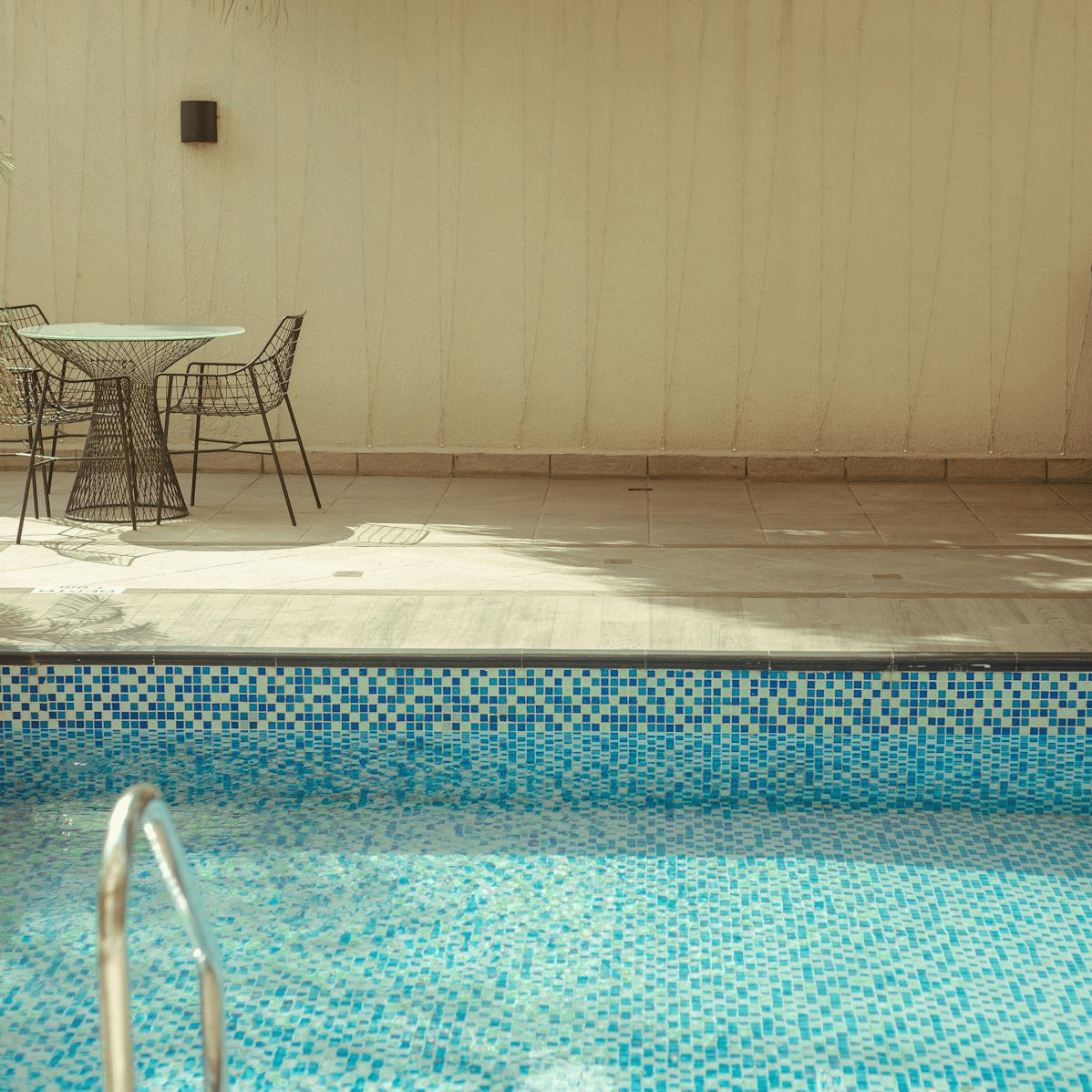 A swimming pool with a lounge chair, a small table with two chairs, and a potted plant placed nearby.
