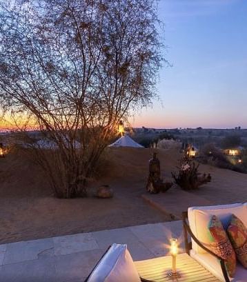 An image of the outdoor seating area shot in the evening with its seating arrangement and sparse vegetation - MANVAR Resort & Desert Camp