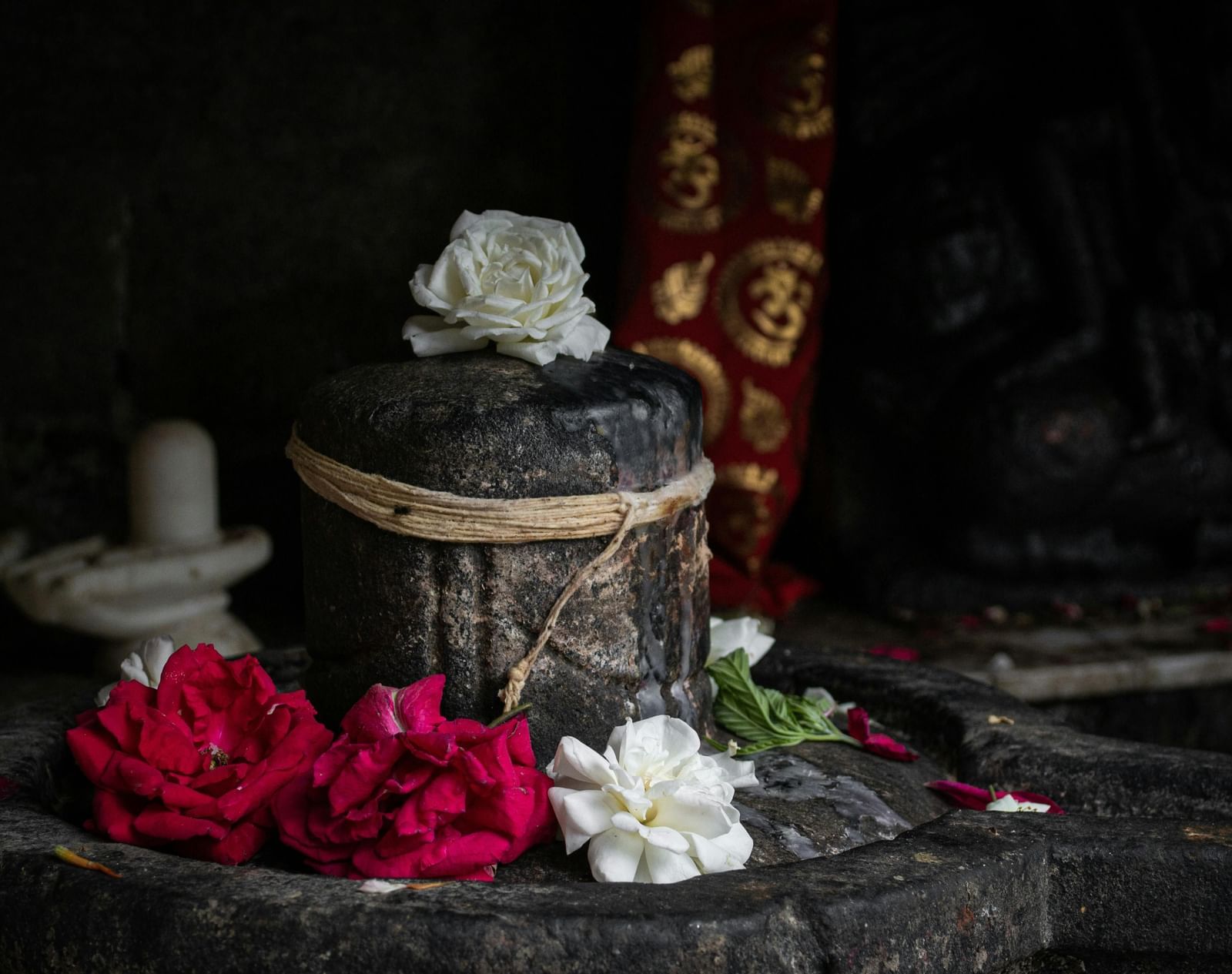 Stone idol adorned with red and white flowers inside a small shrine.