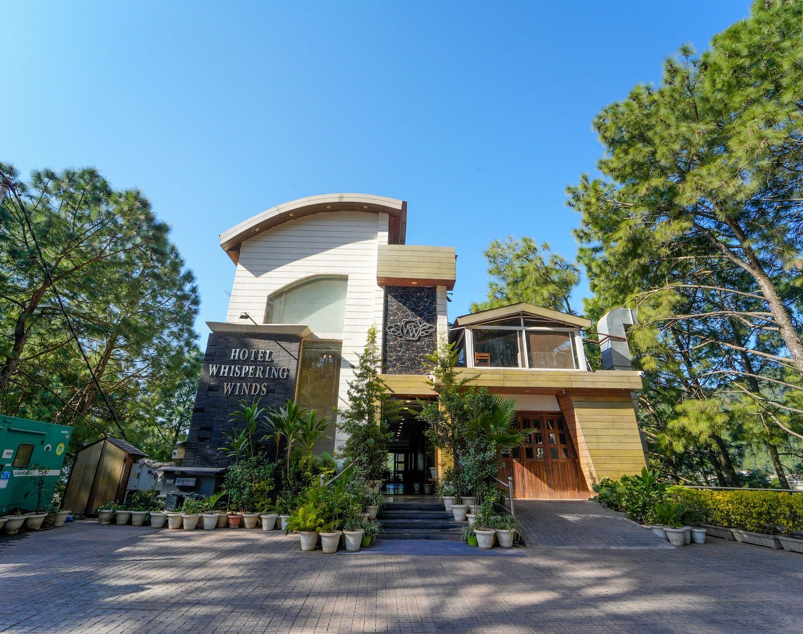 A facade view of, surrounded by trees with a clear blue sky in the background.