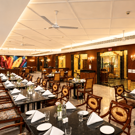 Indoor 1914 restaurant with marble-topped tables, cane-back chairs, wood-panelled walls and feather wall art at MAYFAIR Palm Beach Resort, Gopalpur-on-Sea.