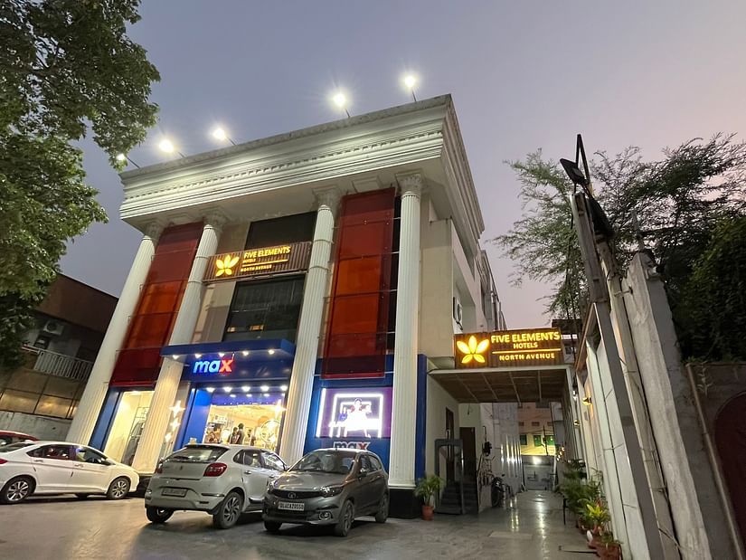 An image of a well lit facade of Five Elements Hotels North Avenue, Delhi which is surrounded by commercial buildings and trees