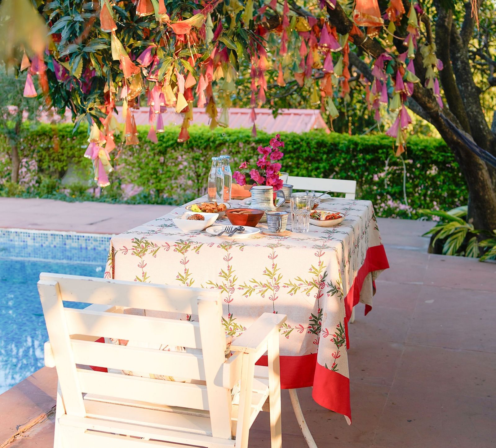 Poolside dining area with a tree decorated with crepe paper on one side, and a table set with a tablecloth and cutlery at Neer Ganga.