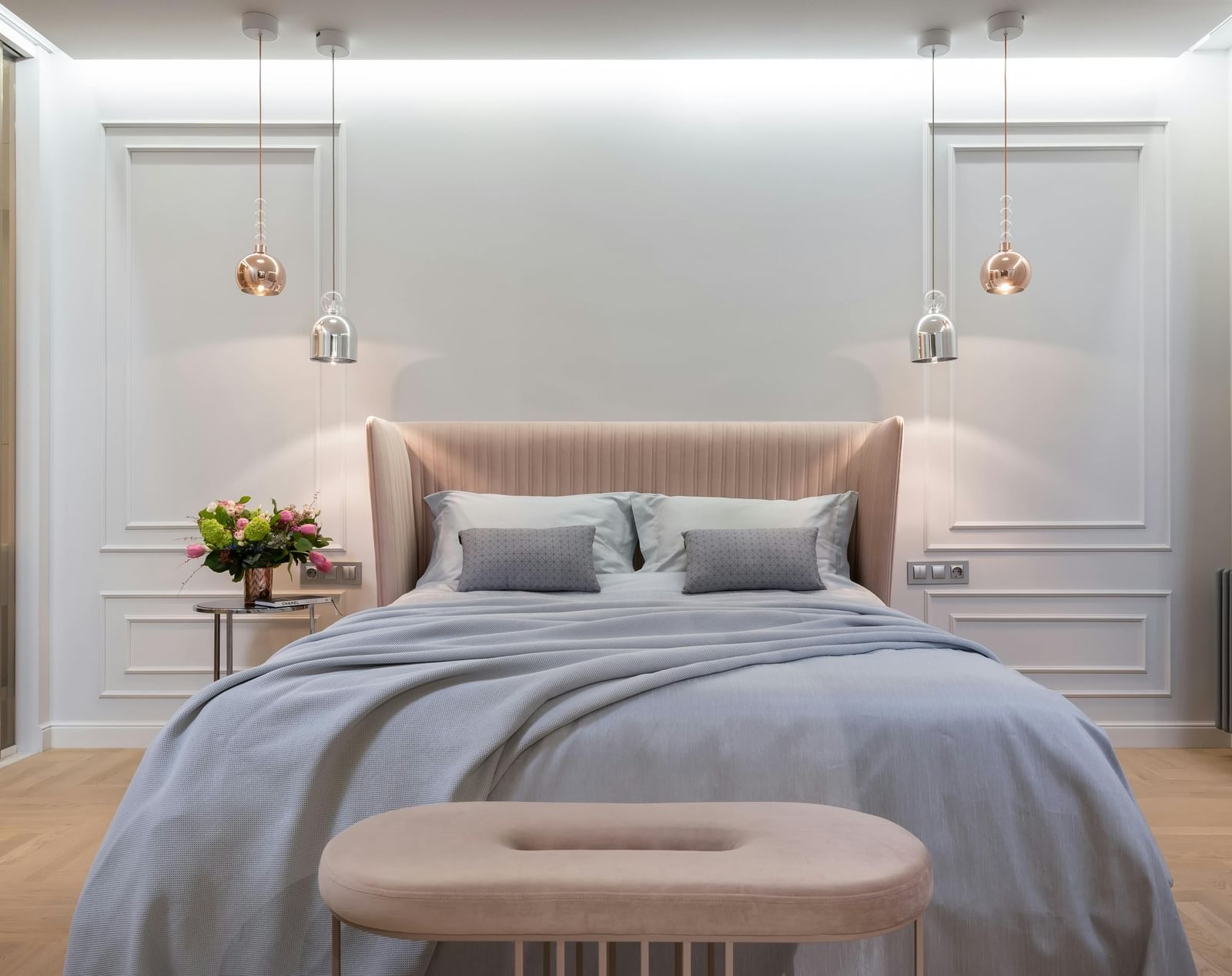 A modern bedroom is shown with soft lighting, a grey duvet, and a tufted bench.