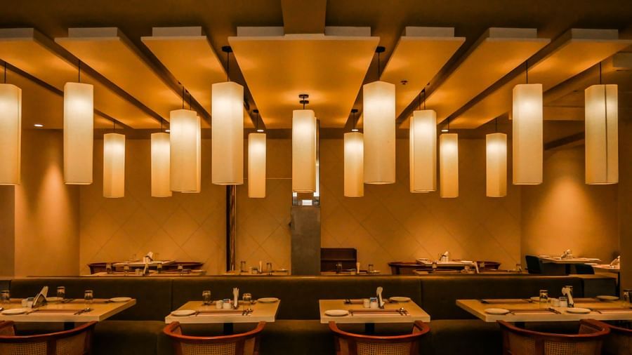 A modern dining area with long tables and unique hanging lights, creating a warm ambience at Shilton Dee Cee.