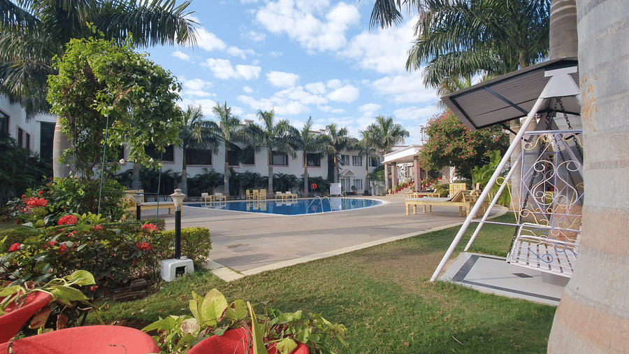 A garden area with a swing, lawn, and palm trees beside the pool at AS Hotels, Khajuraho.