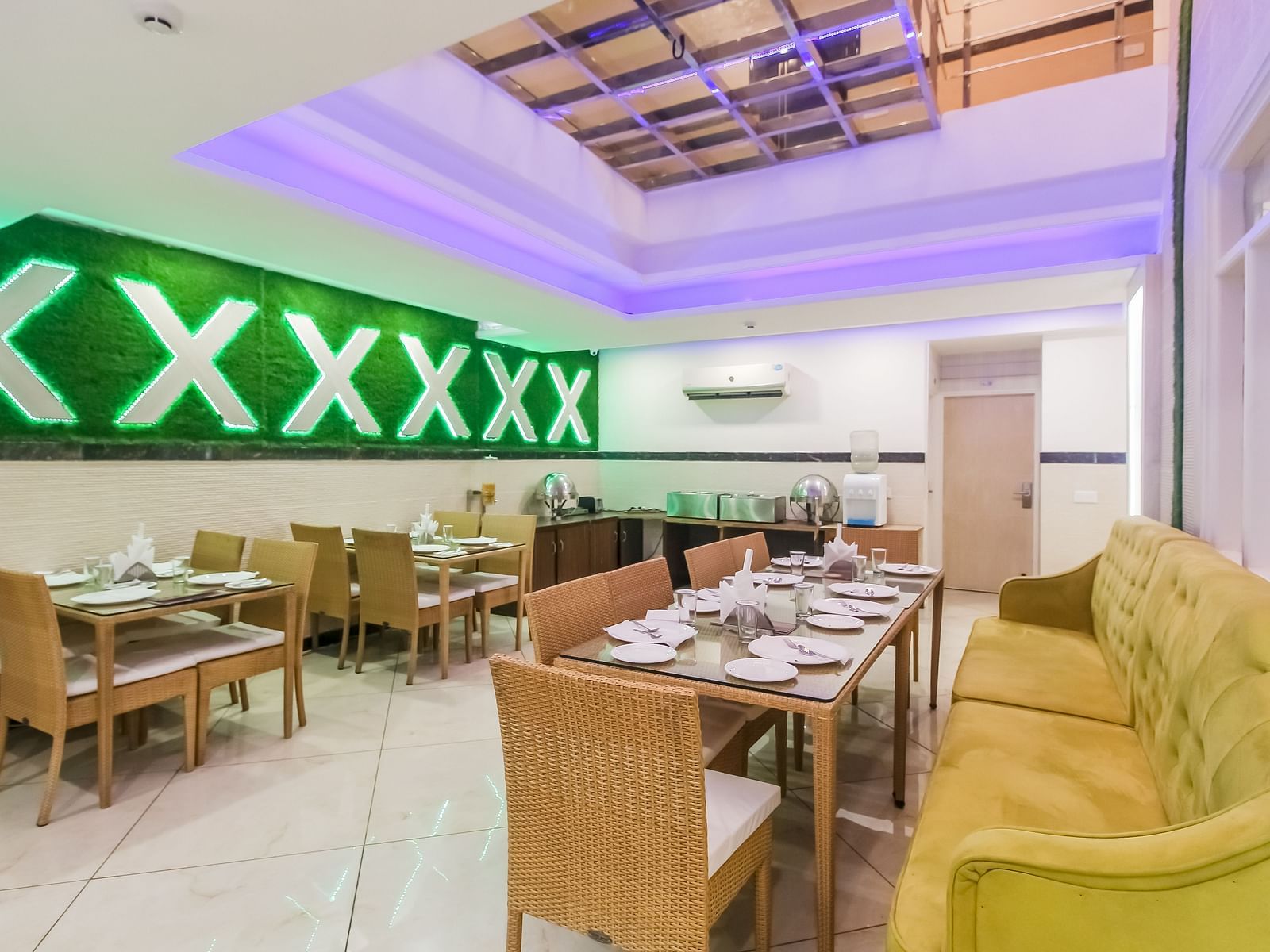 A restaurant interior with a long tufted sofa, wooden tables and chairs, a decorative wall design, and a tiled floor, lit by soft lighting. - Hotel Diamond Plaza, Chandigarh.