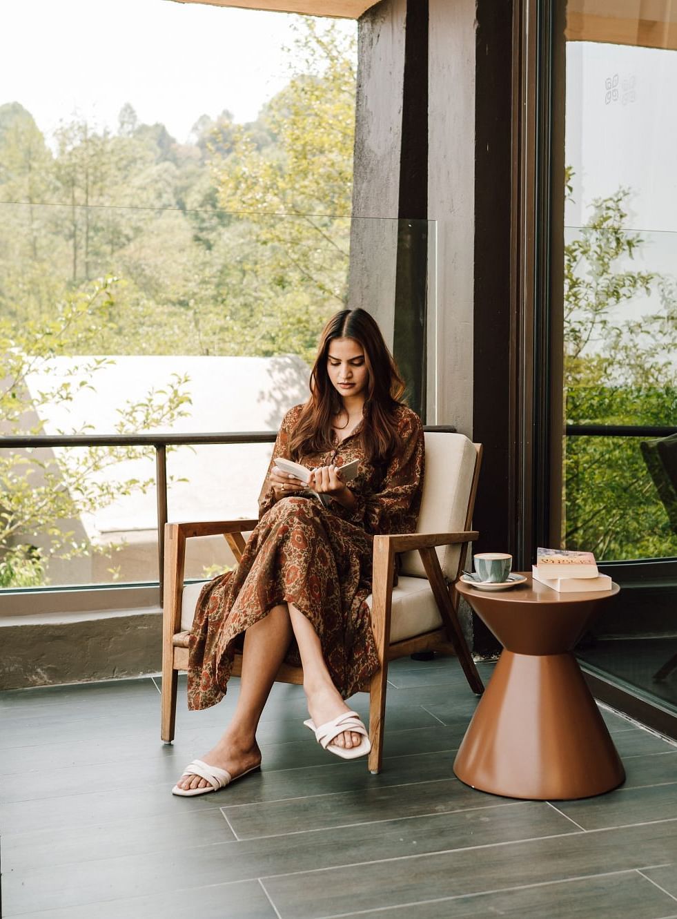 A woman sitting on a balcony, reading a book with a cup of tea beside her.