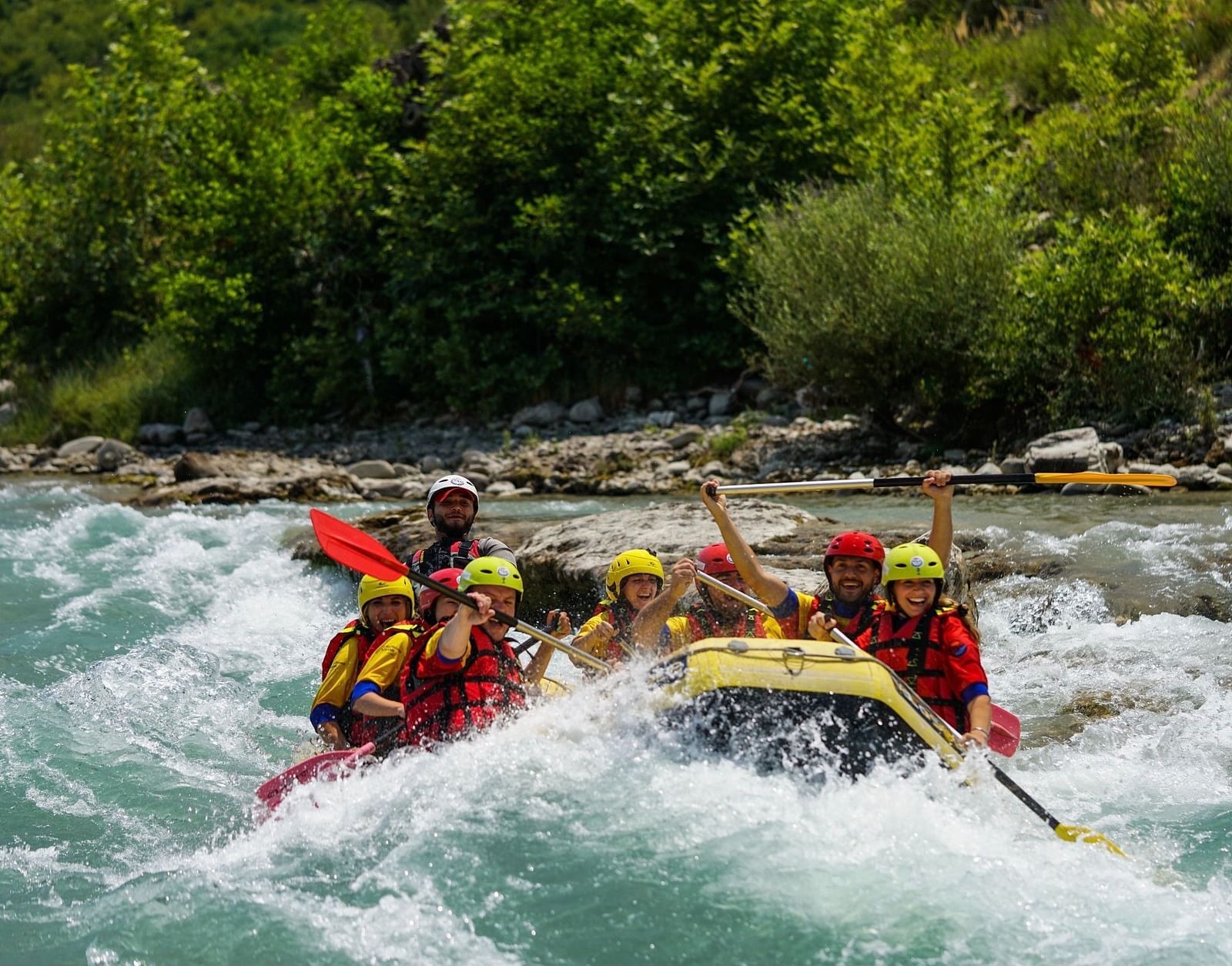 a group of people water rafting on a river with forest cover in the background