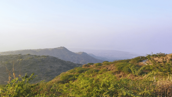 A landscape view of rolling hills and a valley in the distance under a clear sky.