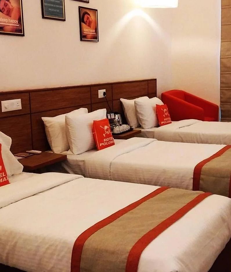 A room featuring three single beds with white linens and brown and red accents at Max Hotel Jabalpur.