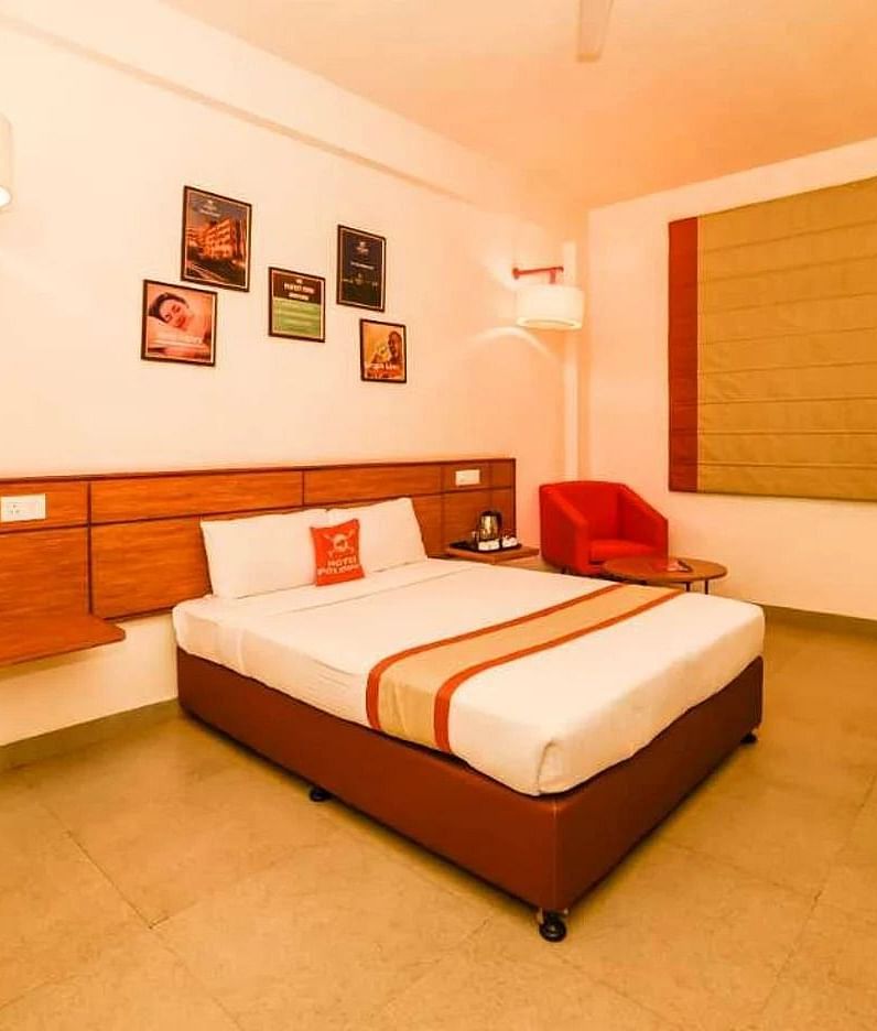A bedroom at Max Hotel Prayagraj, featuring a bed with white linens and a striped bed runner, a wooden headboard, and a desk with a chair.