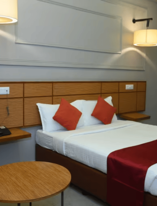 Bedroom with double bed, red runner, pillows, green chair, table and wall lamps at Max Hotel Prayagraj.