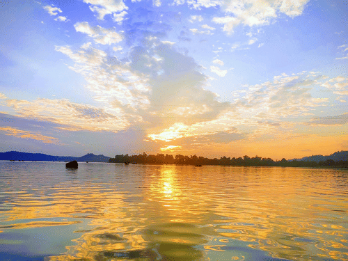 Sunset over lake with calm waters reflecting the sky and distant trees.
