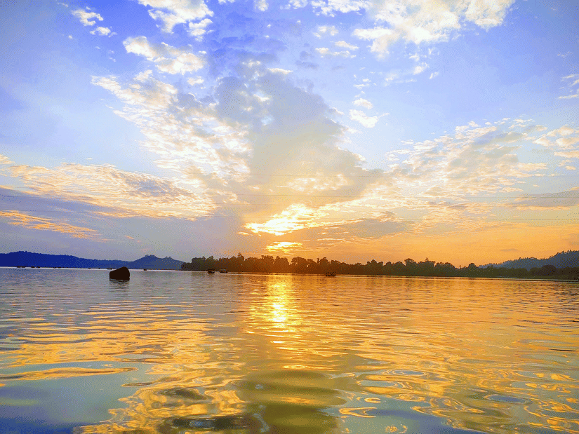 Sunset over lake with calm waters reflecting the sky and distant trees.