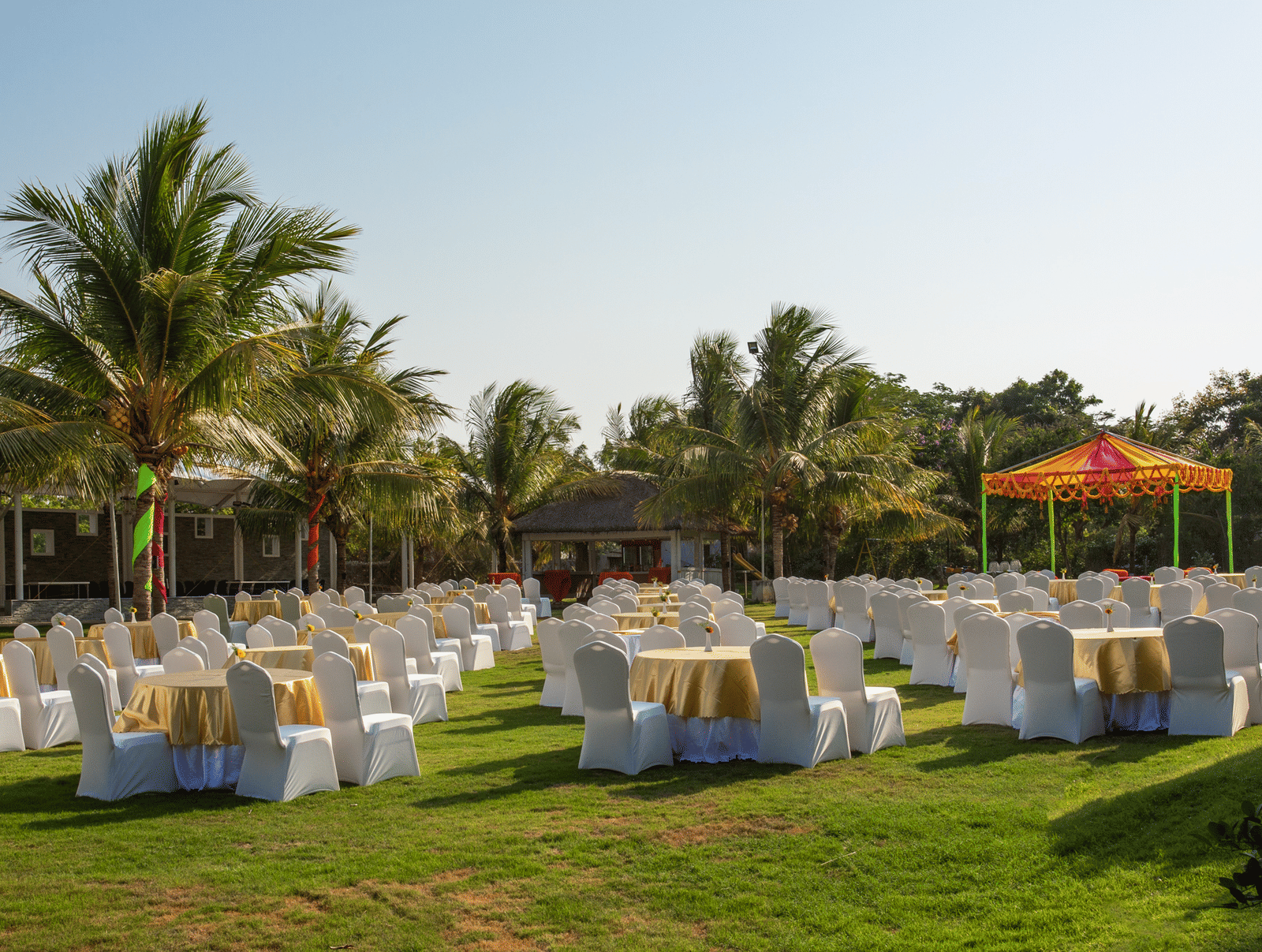 An expansive outdoor event setup on a large green lawn with many tables and chairs draped in white, surrounded by tall palm trees - Grande Bay Resort & Spa, Mamallapuram