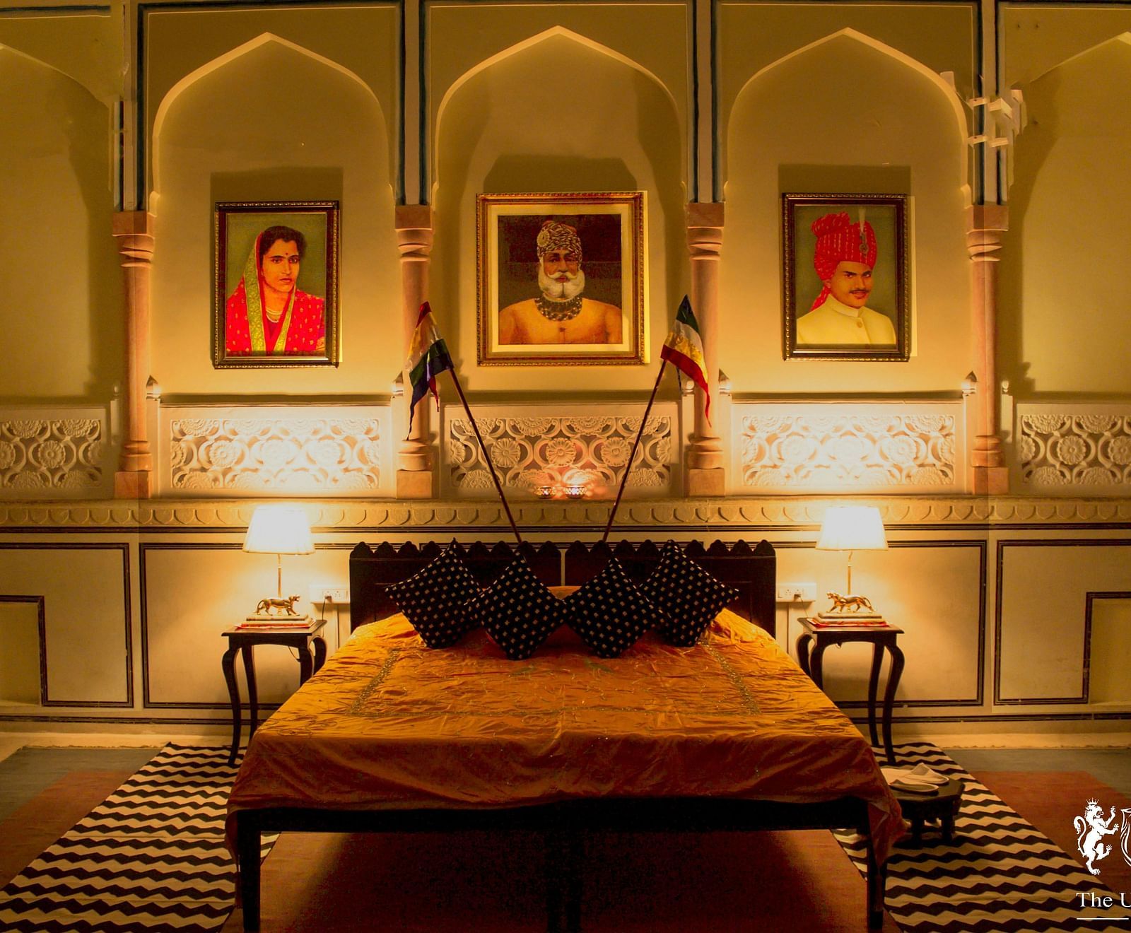 A bedroom at Umaid Vilas Jaipur with a low bed, framed portraits, and arched alcoves in the walls.