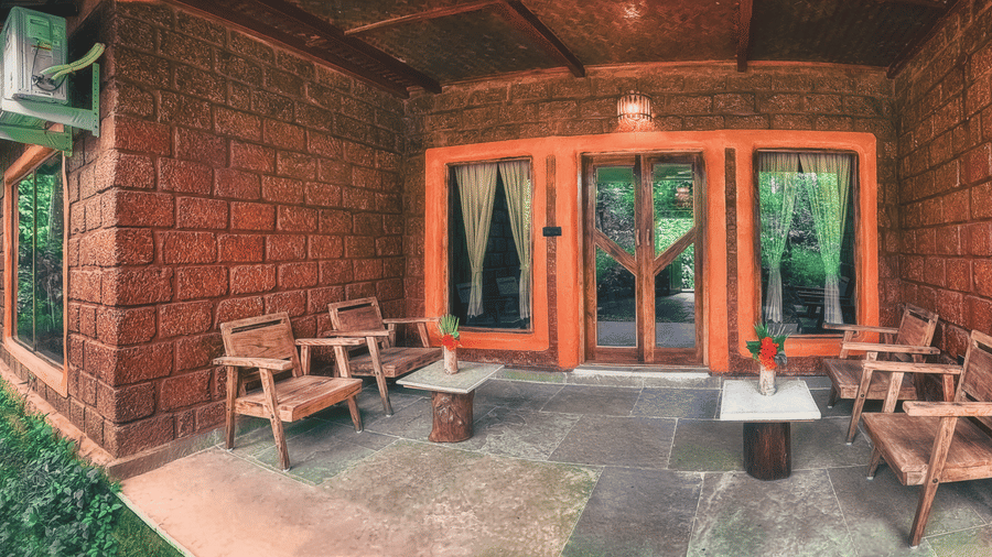 A rustic red-brick cottage porch with wooden armchairs and small coffee tables at Copper Edge - Eco Resort, Coorg.
