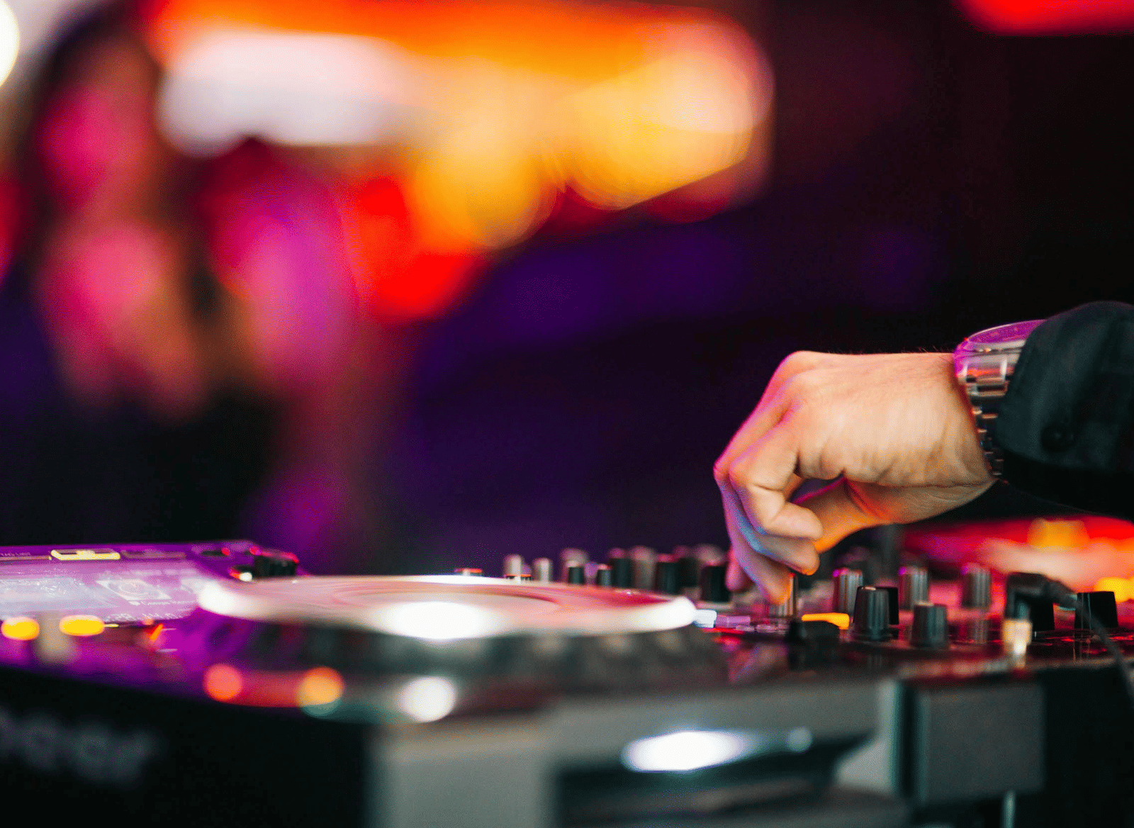 A disc jockey is seen operating a pioneer mixing deck in a illuminated background.