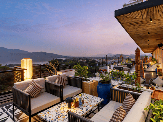 Armchairs and cushioned seating are arranged on a rooftop terrace at The Sierra - By The Lake, offering an open view of hills under an evening sky.