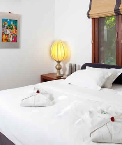 A bedroom with a white bed, white towels shaped like swans, and artwork on the wall - Shreyas Retreat