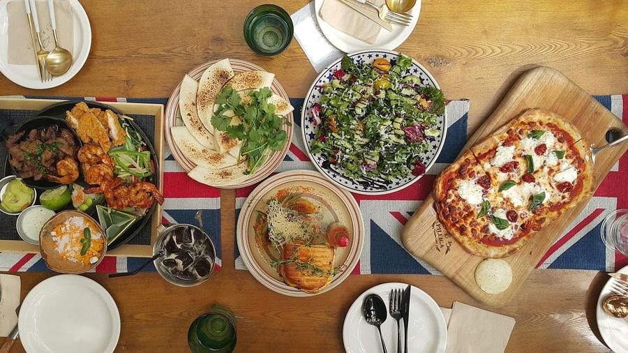 A vibrant spread of pizza, salad, and fish dishes laid out on a wooden table, ready for a meal.