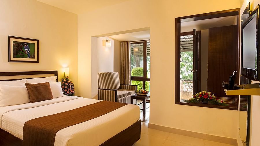 Room with a made-up bed, framed artwork hung on the wall, and a doorway leading to the balcony - Abad Copper Castle, Munnar