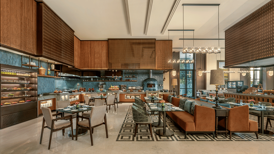 Chithirai restaurant with a show kitchen, wood-fired oven, pastry display, orange banquette seating and geometric floor tiles at The Residency Signature Madurai.