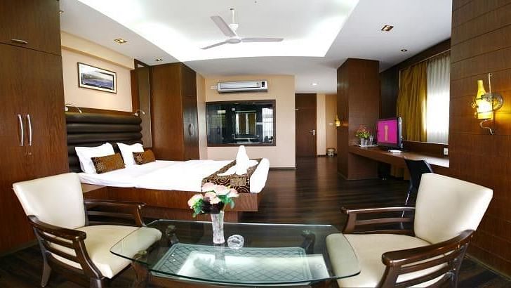 A king size bed with two seats and a coffee table inside Executive Room at VITS Select Grand Inn Ratnagiri