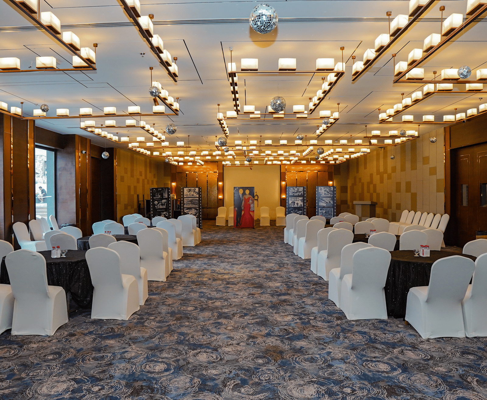 A view of a long event hall set up with multiple rows of chairs for an audience, showing the full length of the room.