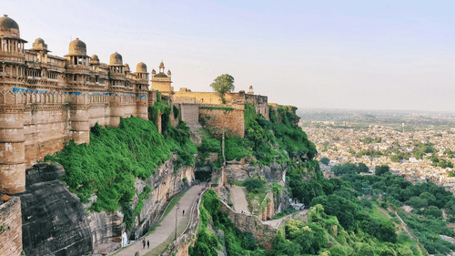 A panoramic view of Gwalior Fort perched on a rocky hill, overlooking the city and surrounding greenery.