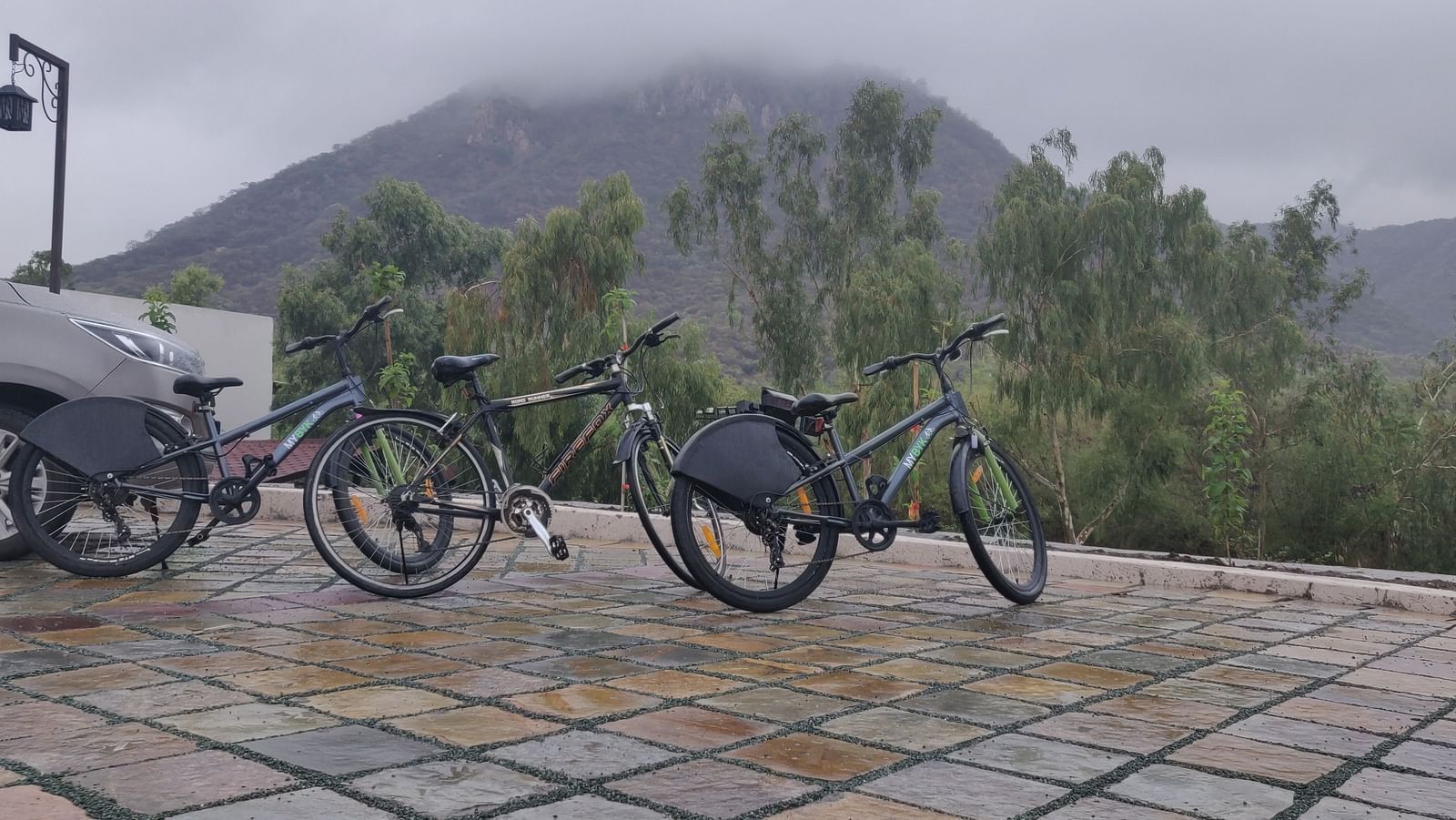 Two bicycles parked on a paved area, with a car visible on each side. - Bamboo Saa Resort & Spa, Udaipur
