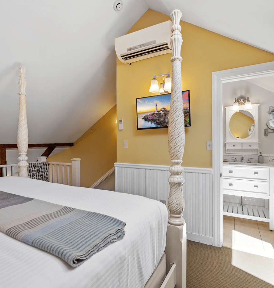 A wide view of a cozy guest room with a four-poster bed, yellow walls, and a bathroom doorway.