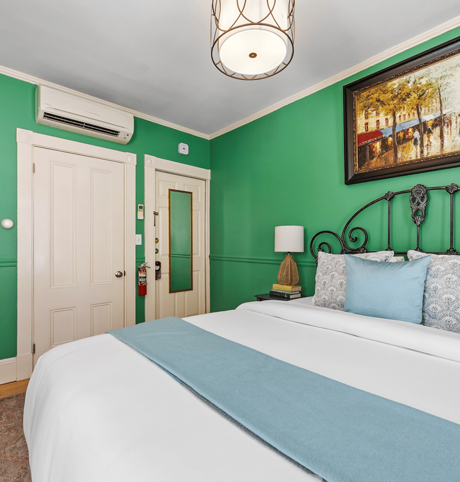 A wide-angle view of a guest room with a green accent wall, a white door, and a bed with a black metal frame.